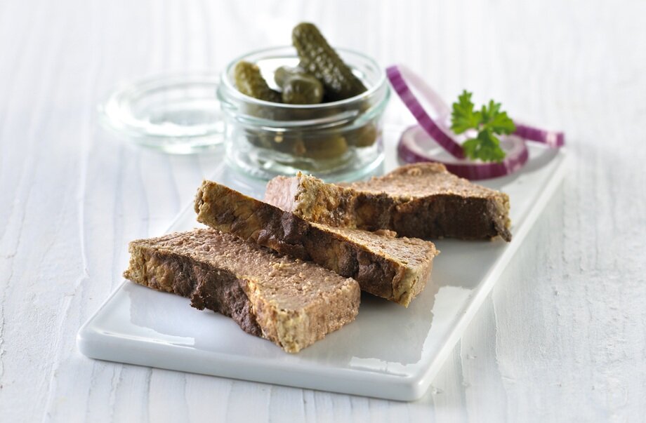 Leverpostei med sylteagurk og rødløk på et skjærebrett.